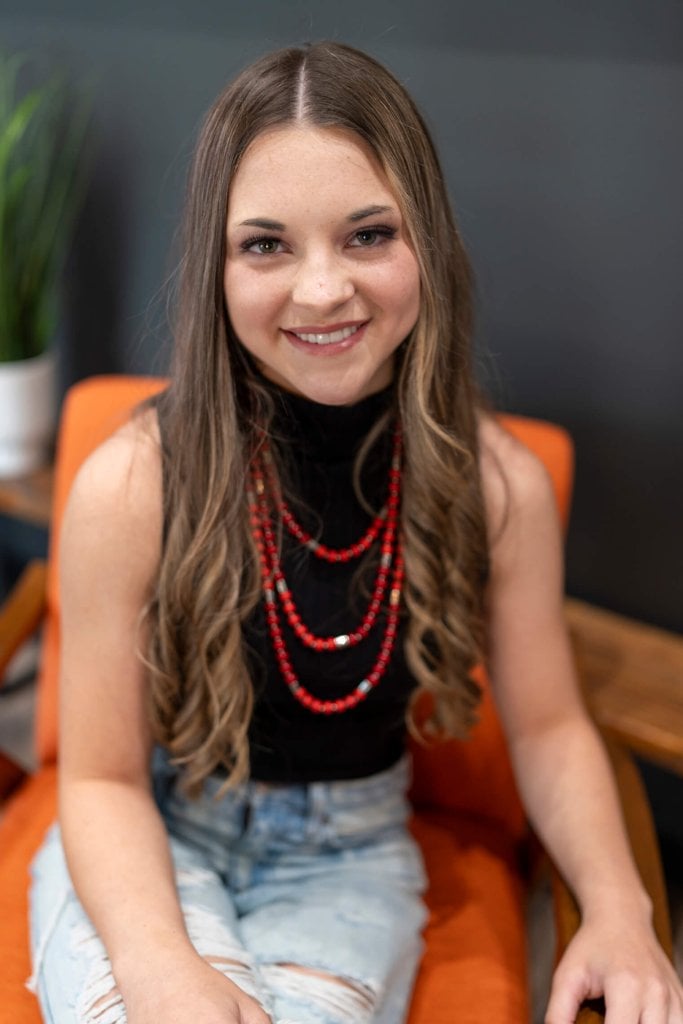 A young woman experiencing relief from TMJ pain while sitting in an orange chair with a red necklace.