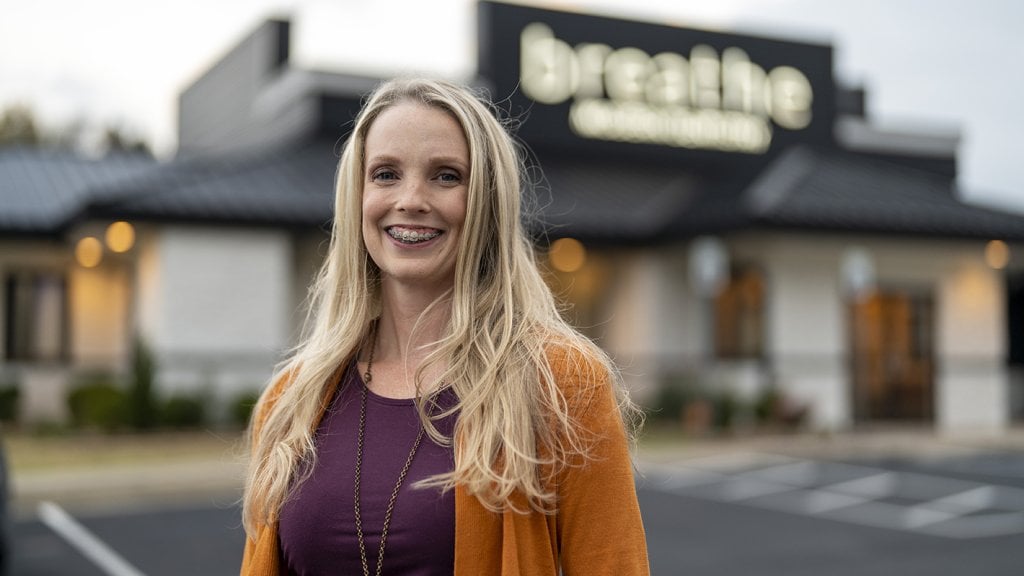 A woman smiling in front of a restaurant, experiencing TMJ relief.
